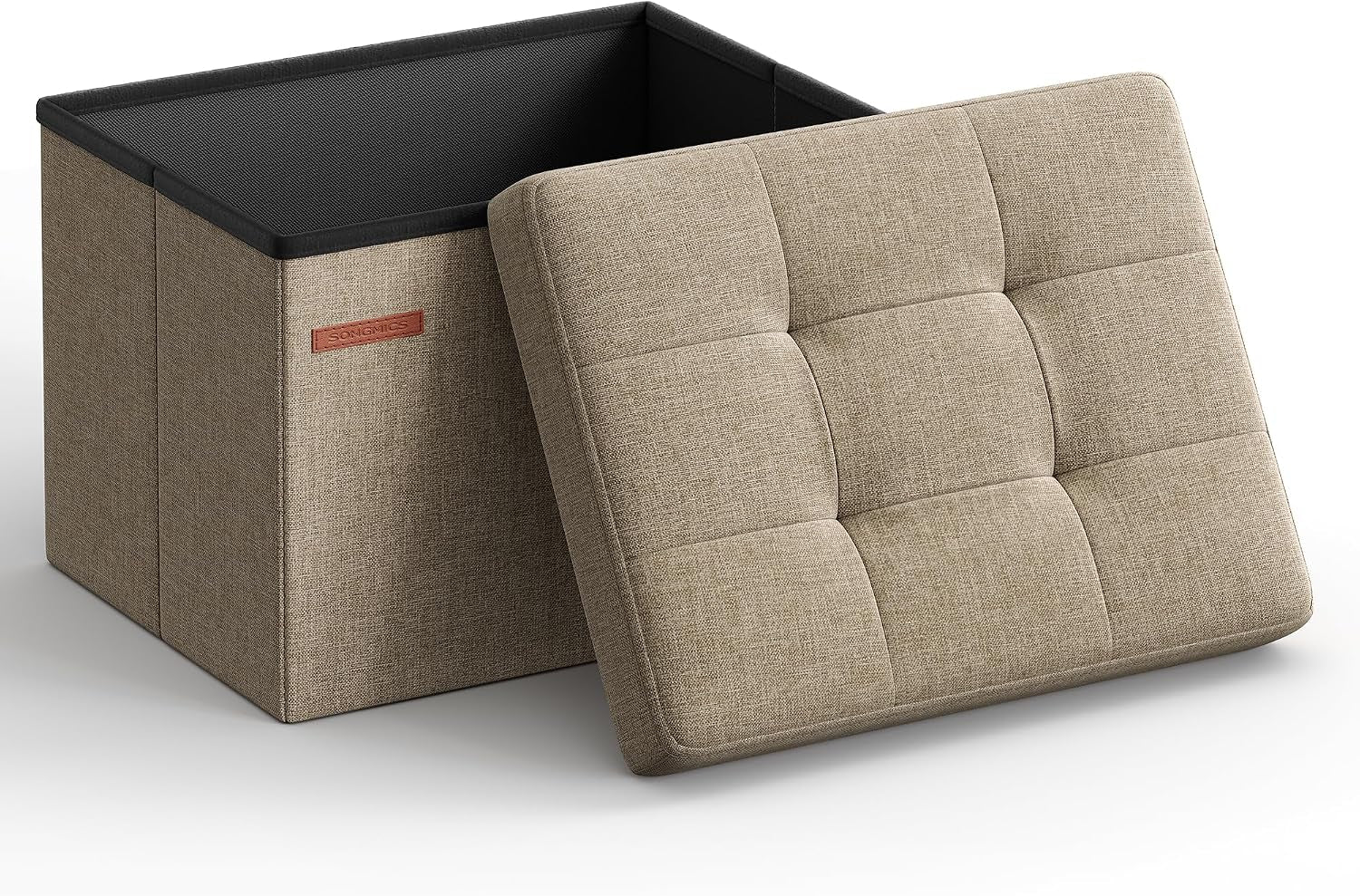 Three-quarter view of a beige/tan fabric folding storage ottoman with its tufted lid leaning against the open box