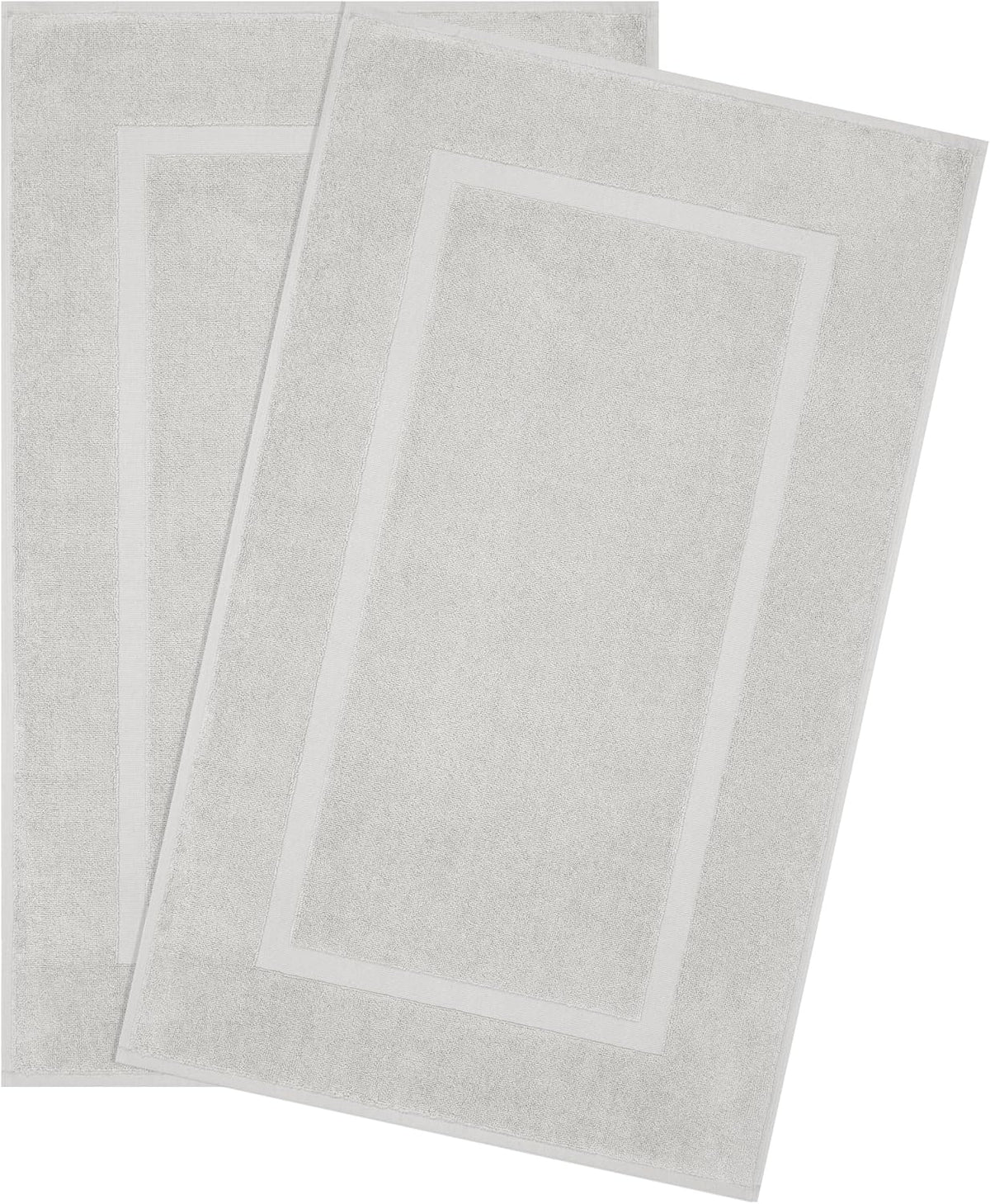 Two snow-white rectangular bath mats with a simple bordered design, layered slightly askew.