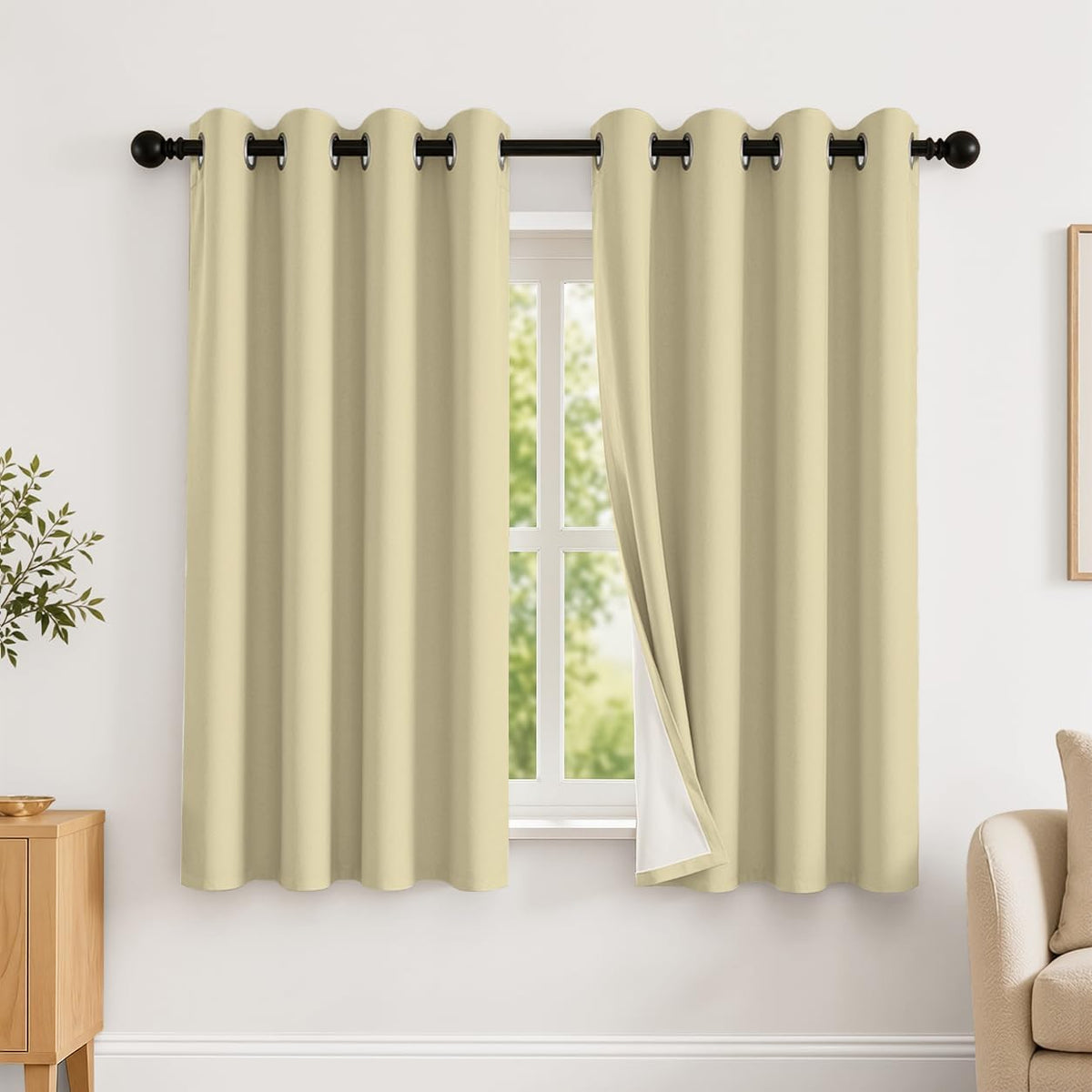 Window with two light cream grommet curtains hung on a black rod, one panel slightly pulled to show white backing.