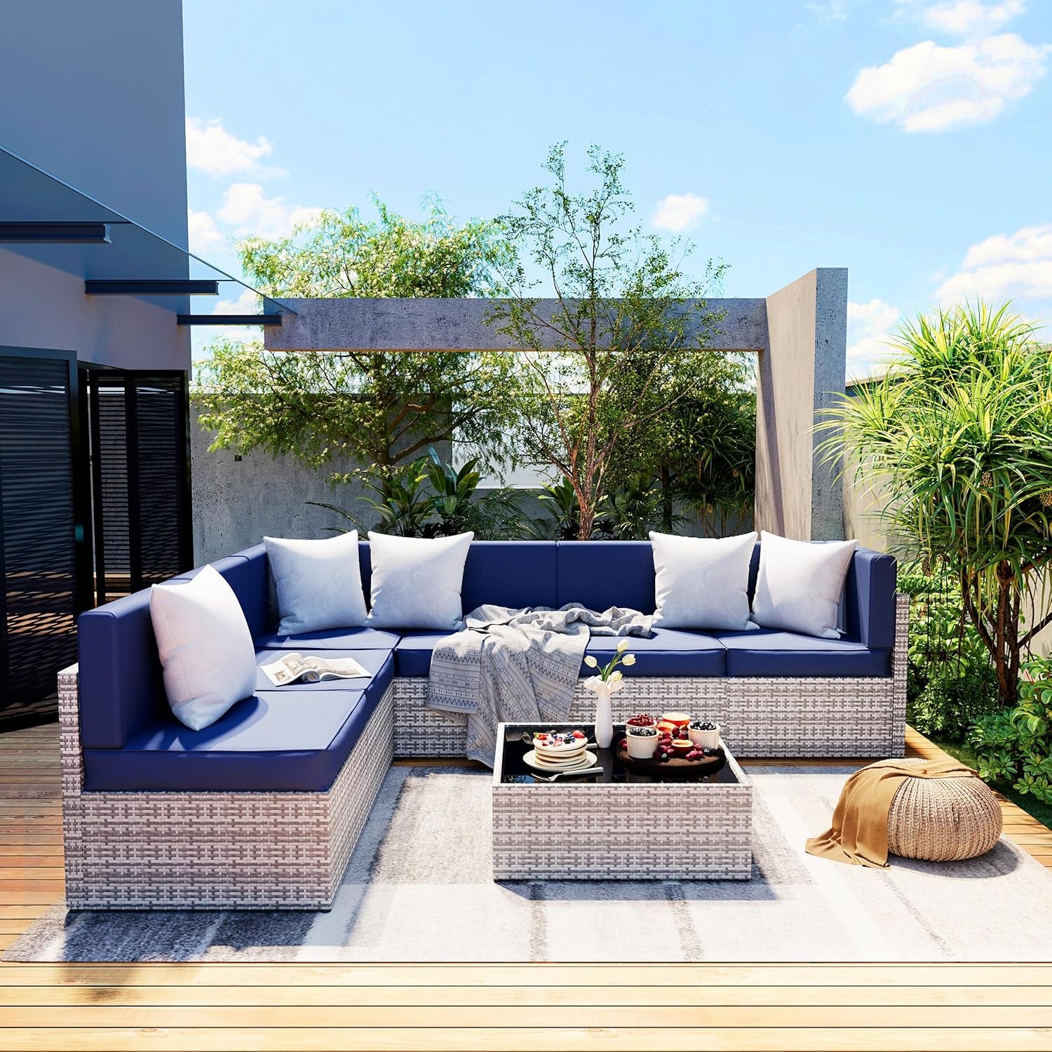 Outdoor corner wicker sectional with deep navy cushions, low wicker coffee table and decorative throw on a striped rug.