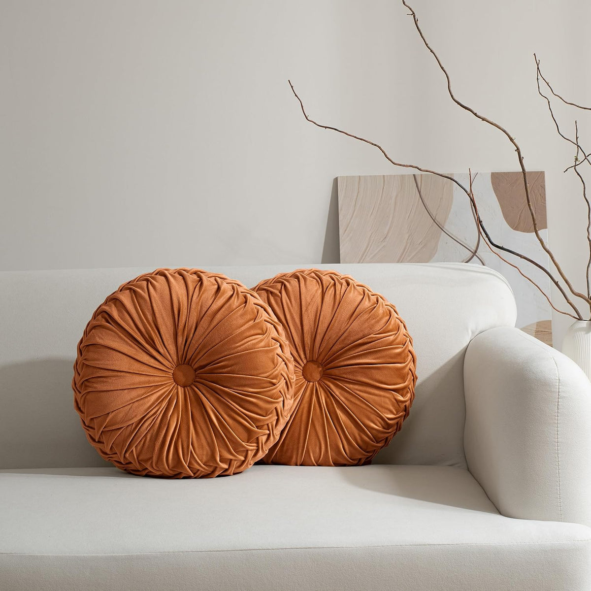 Pair of round burnt-orange ruched pillows arranged side-by-side on a light sofa back.