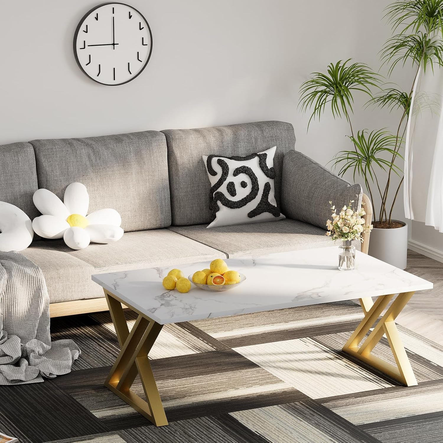 Low white faux marble coffee table with gold X-leg base placed on a patterned rug next to a gray sofa