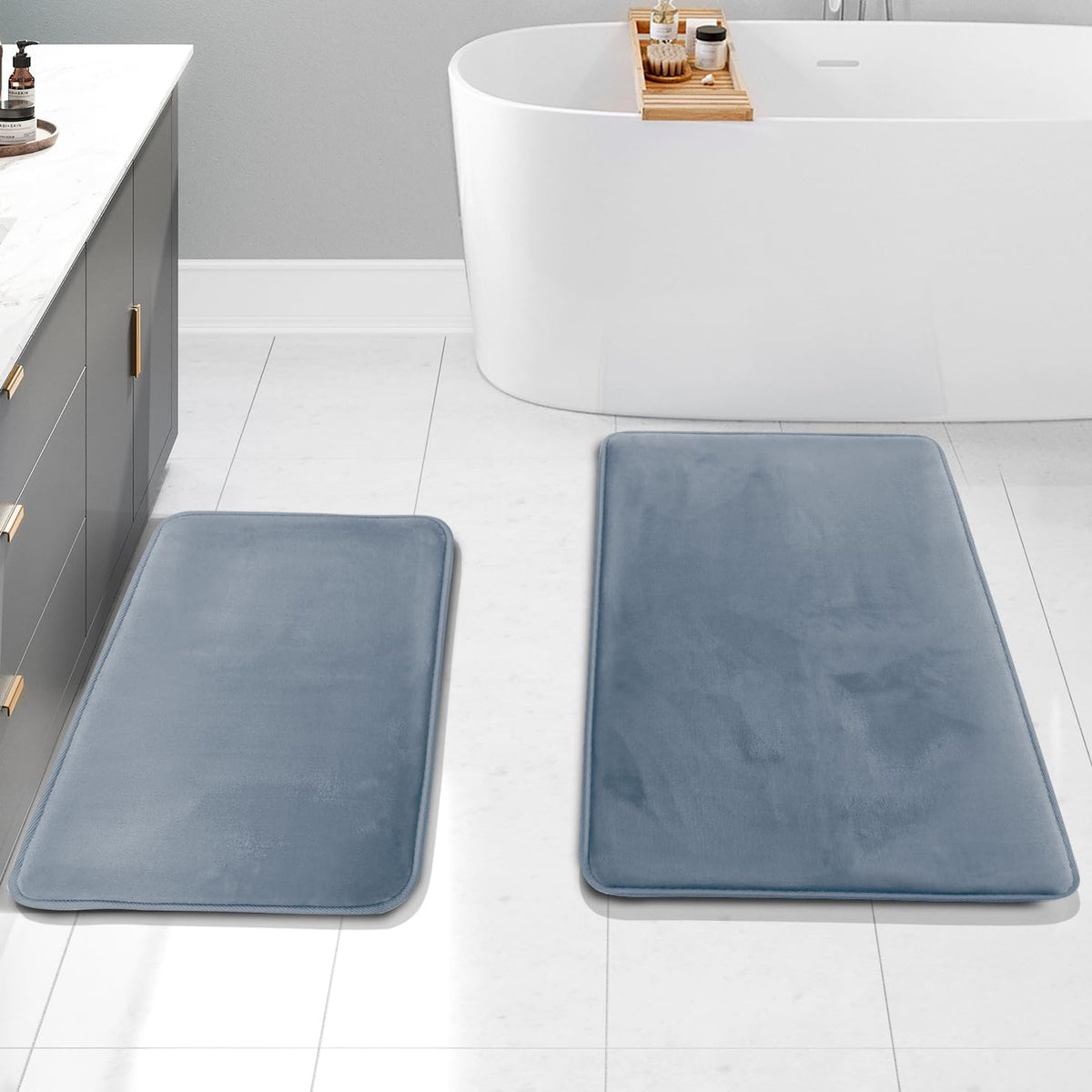 Overhead bathroom view showing two stone-blue rectangular mats placed on white tile in front of a gray vanity and