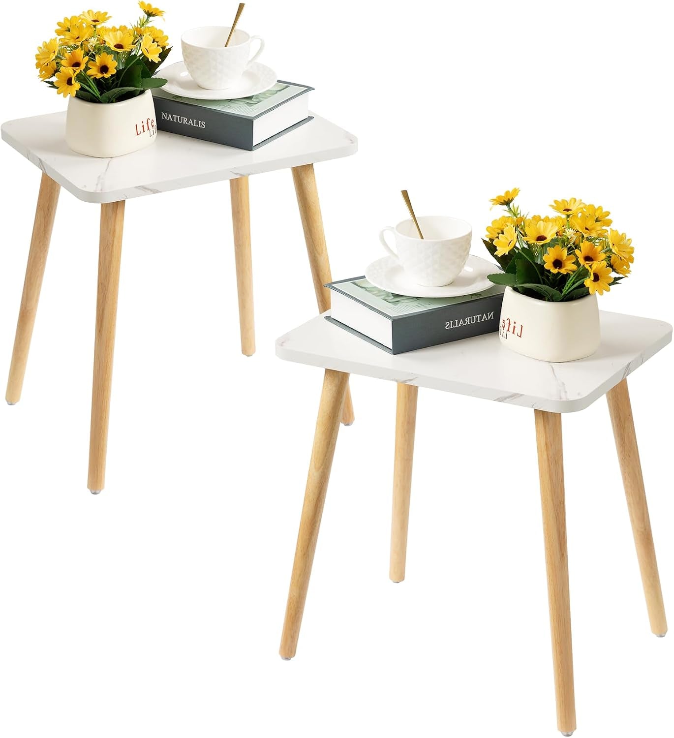 Two white-top side tables with light wood legs shown side by side, each topped with a book, cup, and yellow flowers.