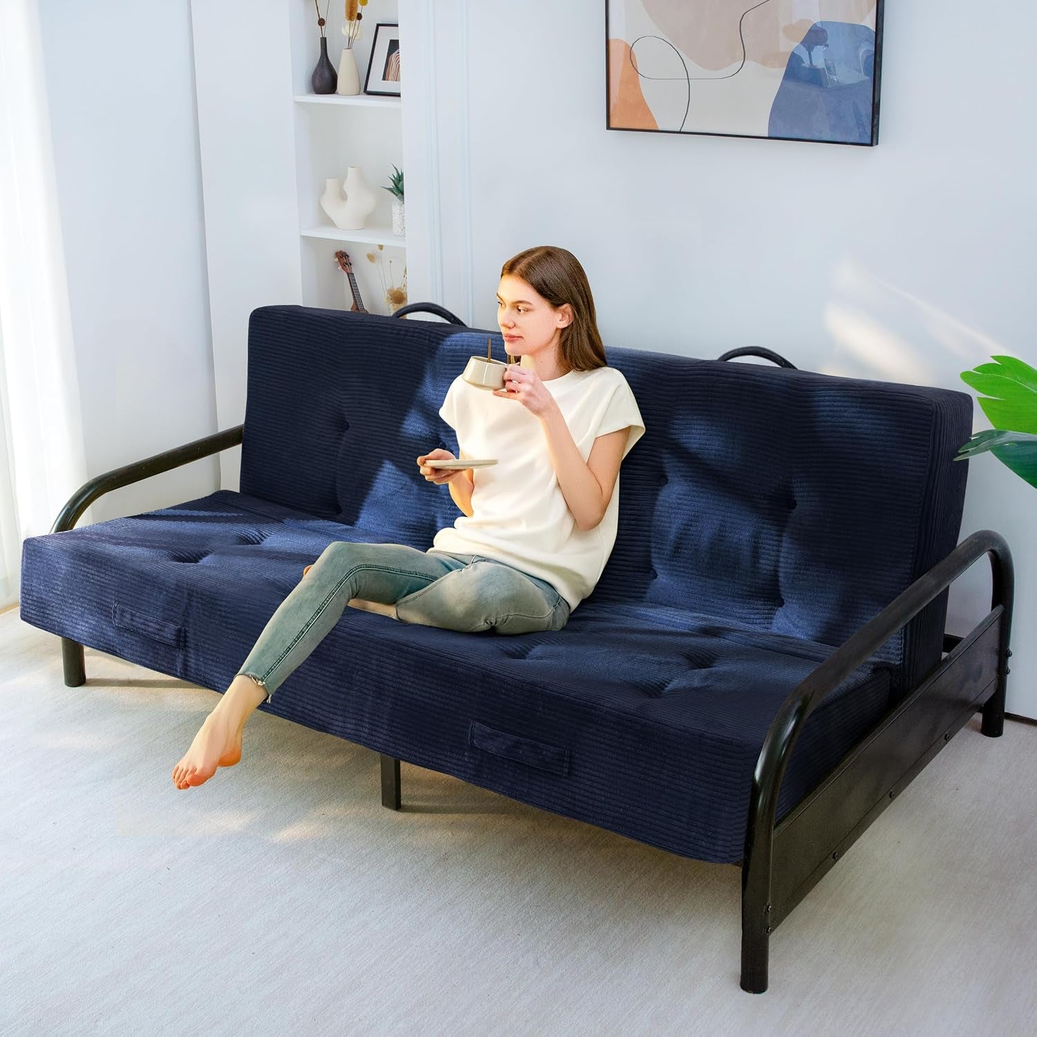 Woman relaxing on a navy corded futon mattress on a black metal frame, holding a cup
