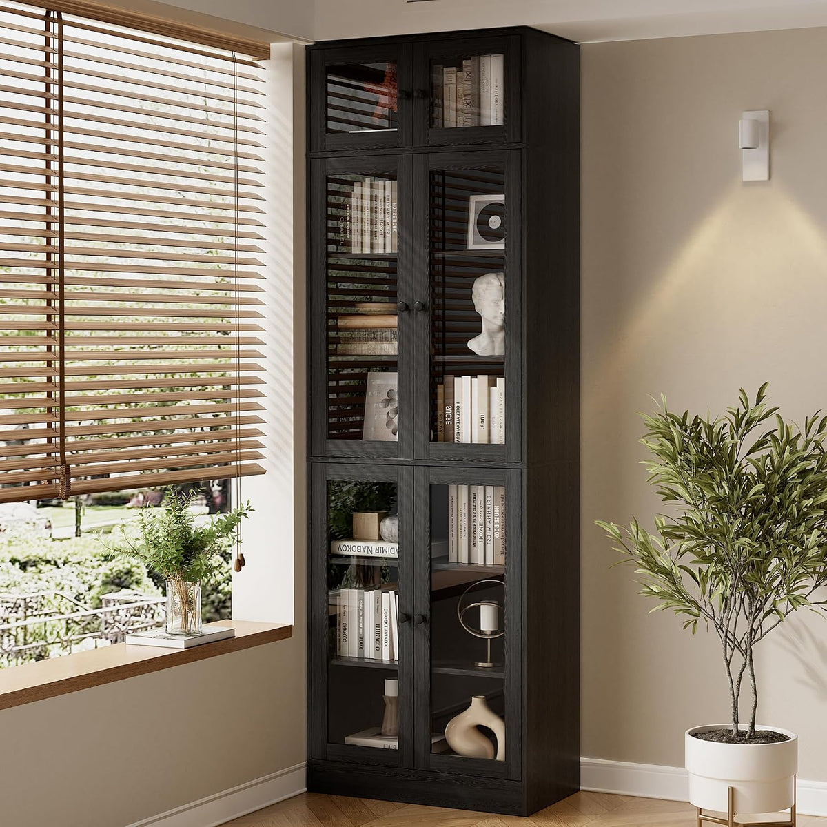 Corner view of a single black bookcase next to a window and potted plant, showing glass-front shelves.