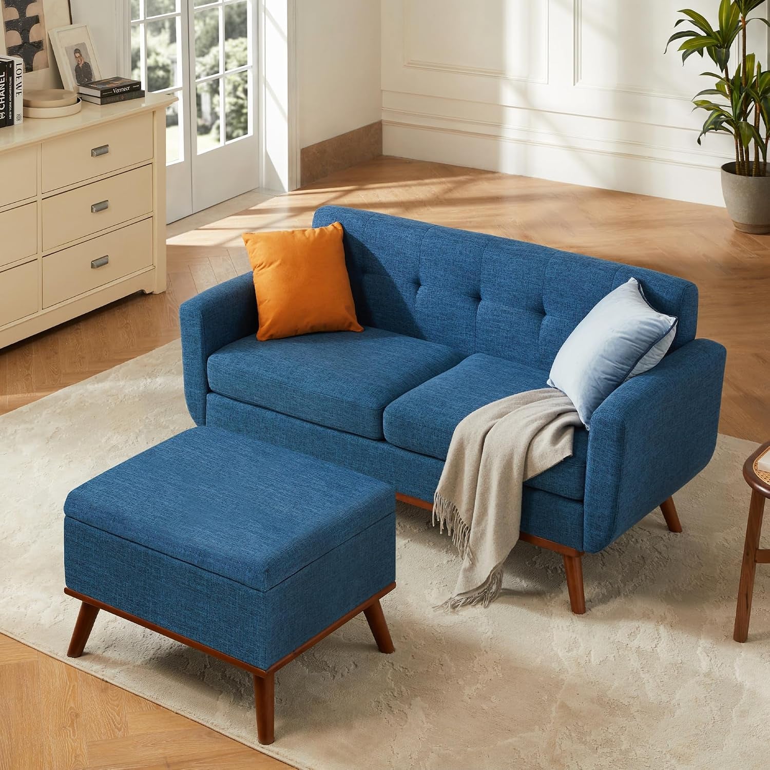 Angled shot of a blue loveseat with an ottoman in front, orange and light blue pillows and a beige throw