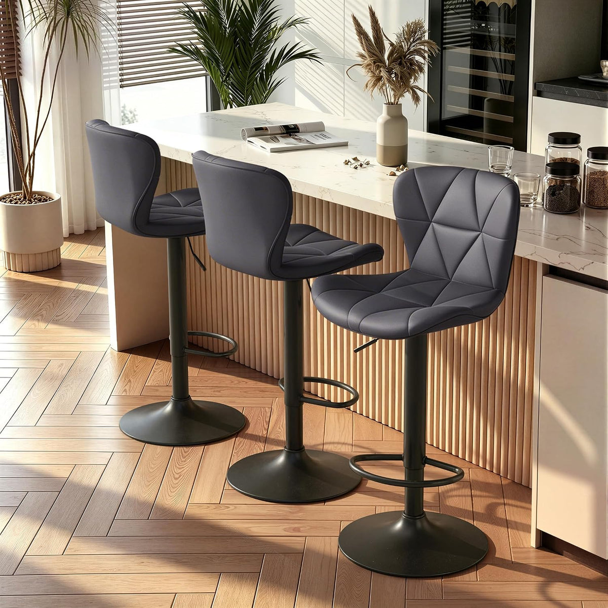 Three dark gray stools at a breakfast bar with sunlight on herringbone wood floors and potted plants nearby.