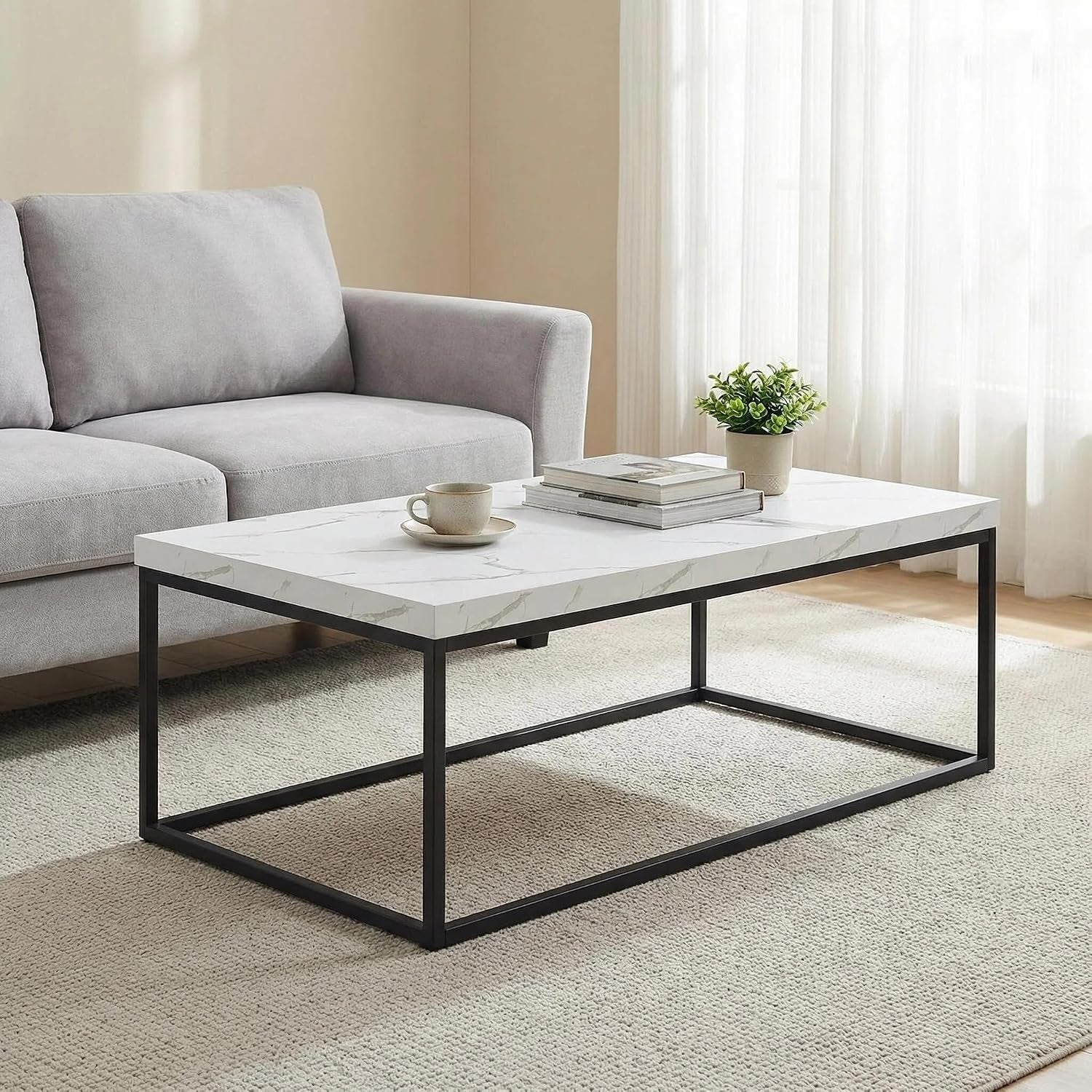 Living-room view of white marble-look rectangular coffee table on a textured rug with a cup, books, small plant and sheer