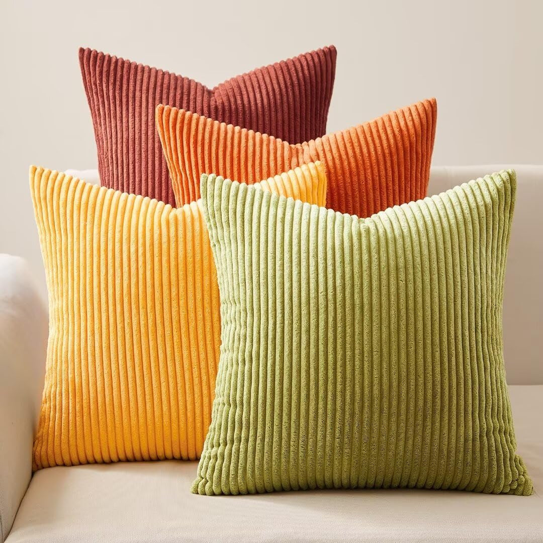 Four corduroy striped square pillows in green, yellow, orange and rust arranged on a light sofa
