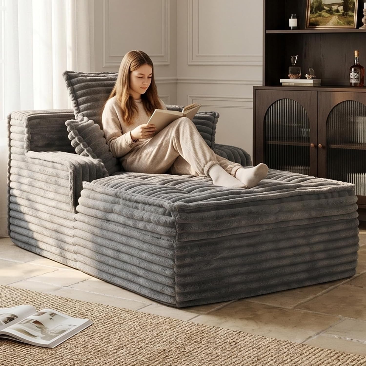 Grey corduroy chaise lounge in a living room with a woman reading and three matching pillows.
