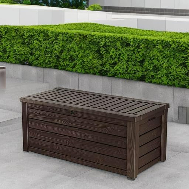 Brown wood-textured resin deck box placed on a patio against a low wall and greenery