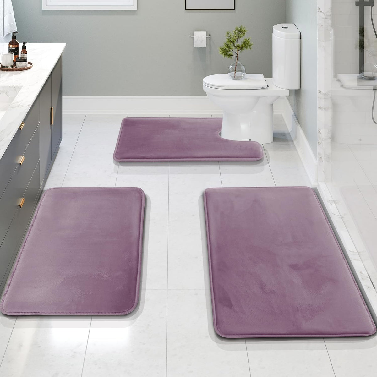 Bathroom scene showing three purple memory-foam bath mats on a white tile floor.