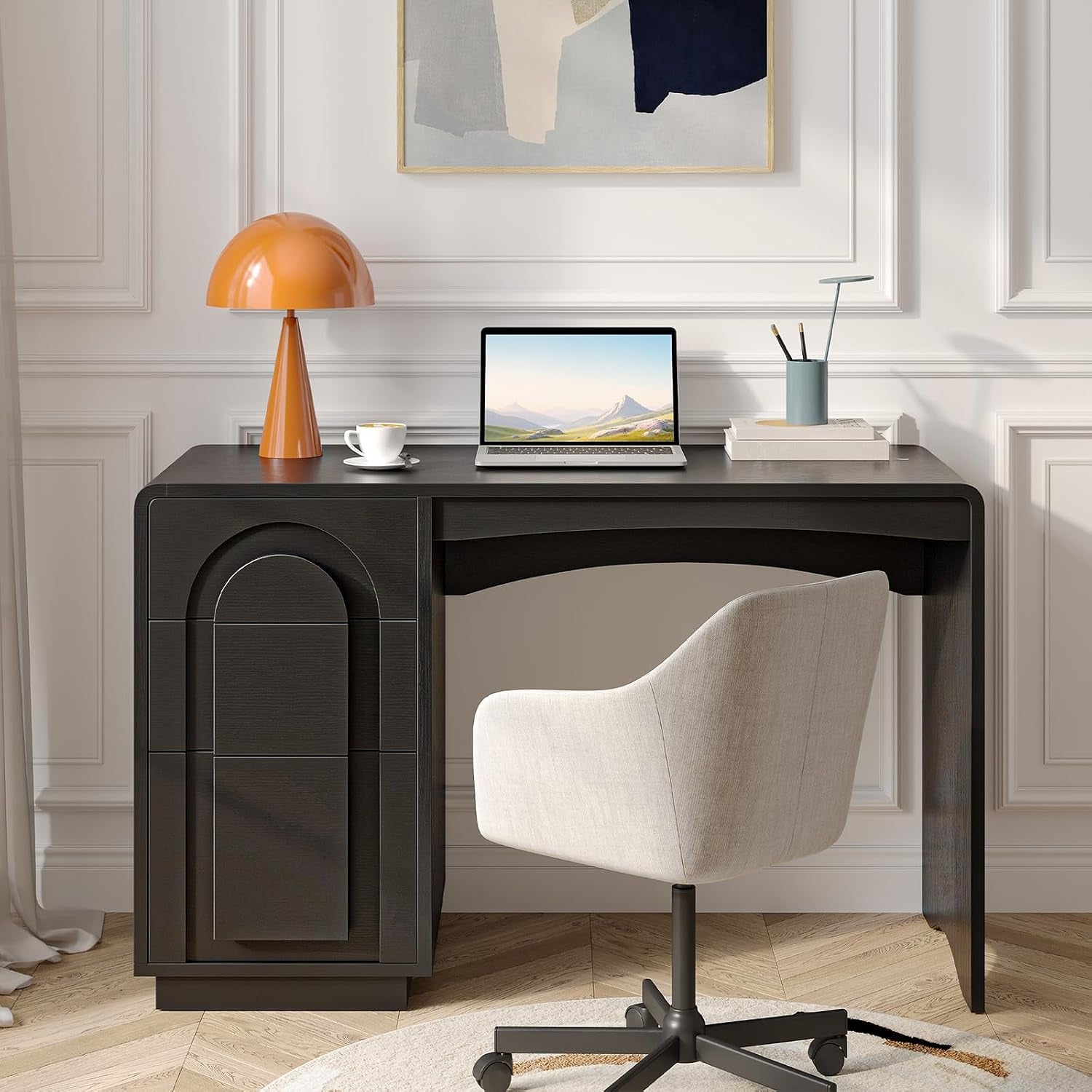Front view of the black desk in a styled room with an orange lamp, laptop, and beige swivel chair