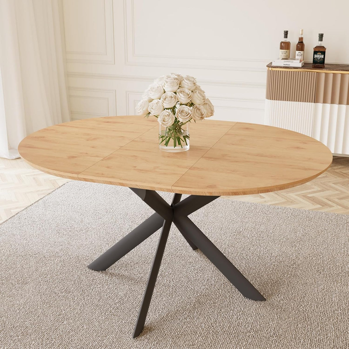 Close-up of round light-wood tabletop and cross-legged black metal base with vase of white flowers.