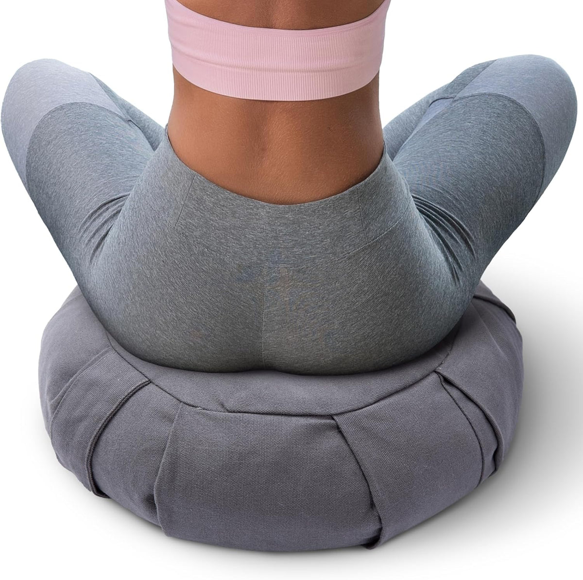 Rear view of a woman sitting on a stitched, pleated gray meditation cushion showing the cushion's paneling.