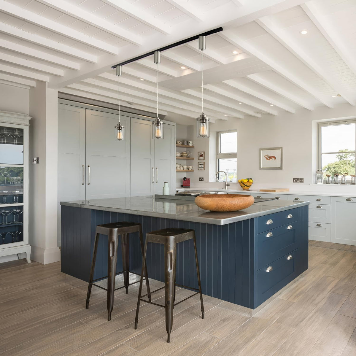Bright kitchen scene with three brushed-nickel track pendants hanging over a large island from a black H-type track