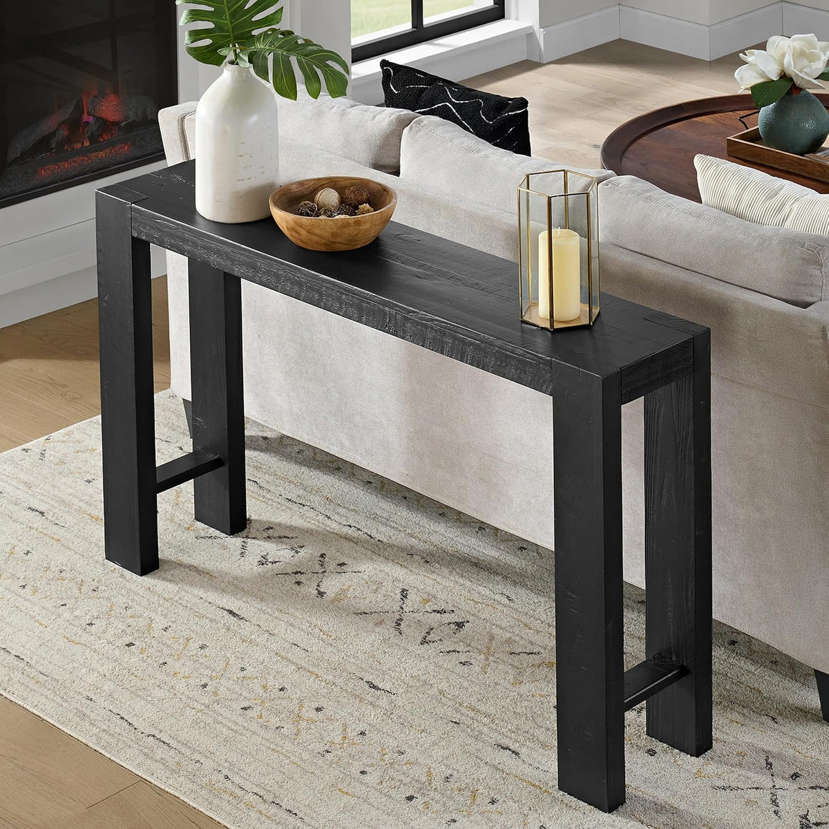 Black-finished console table behind sofa styled with a candle lantern and wooden bowl on top.