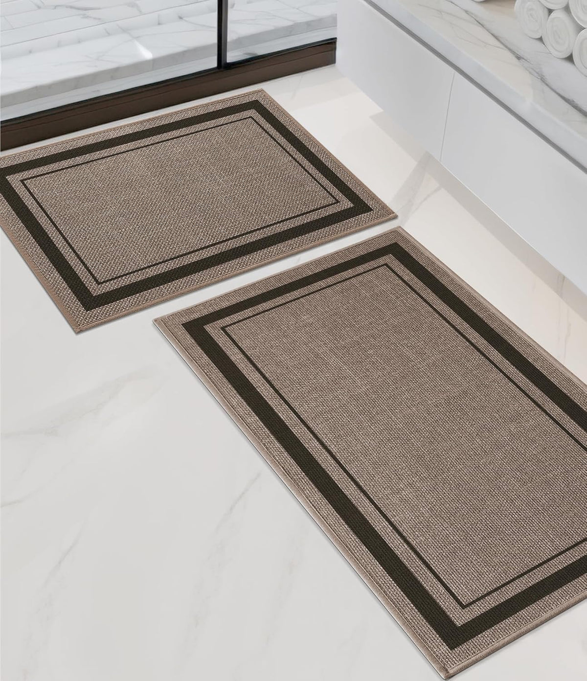 Beige two-piece bath rug set arranged on white marble floor beside a vanity, angled top view