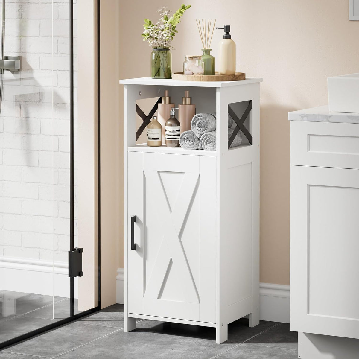 Tall white bathroom cabinet with X side panels next to a sink, styled with bottles and rolled towels on the open shelf