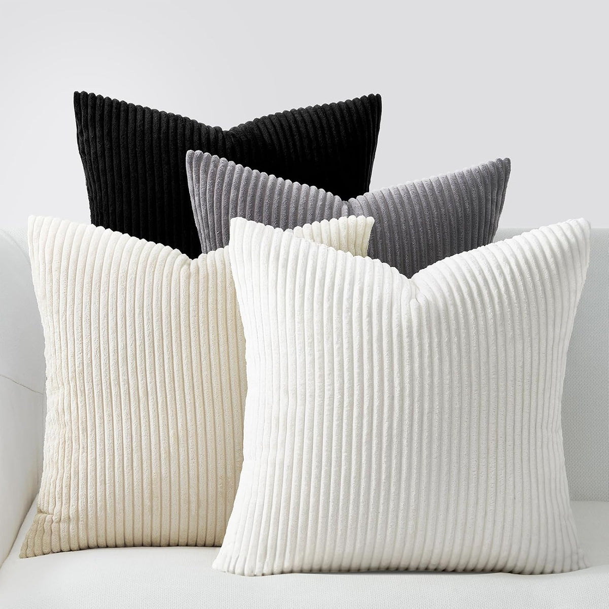 Five ribbed corduroy pillows in black, gray, cream and white grouped on a sofa