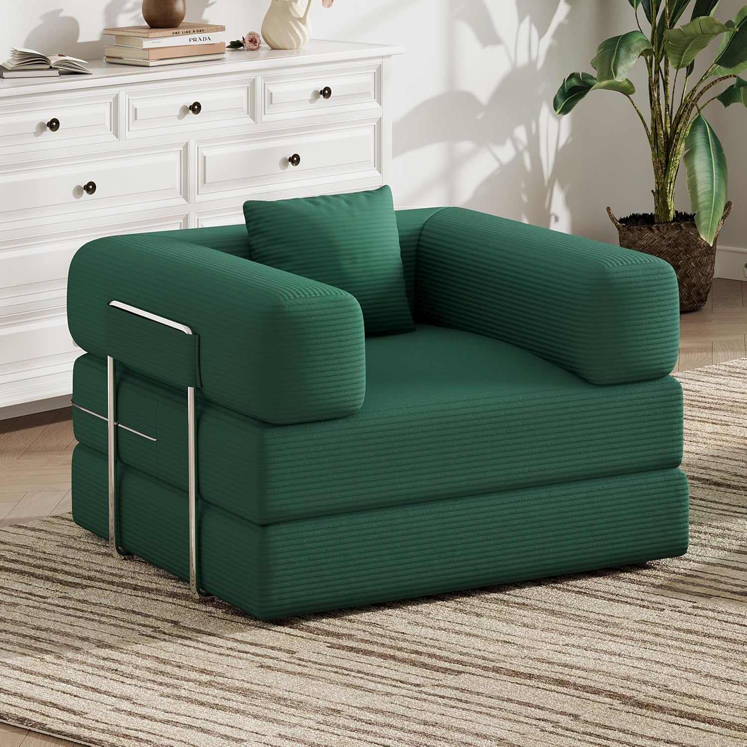 Green corduroy two-seat convertible floor sofa shown angled in a bright room with dresser and plant.