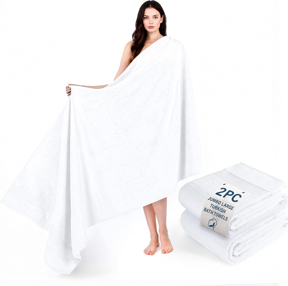 Woman holding a large white bath towel draped around her body with folded white towels at her feet.