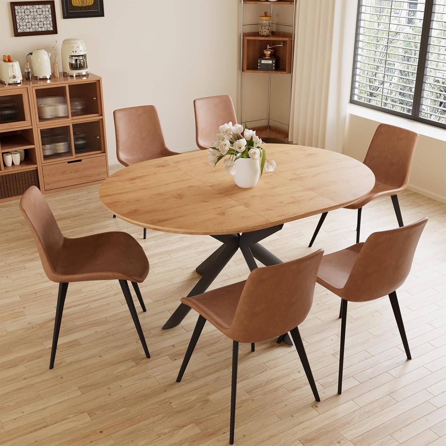 Oval wood dining table surrounded by six brown chairs in a bright kitchen with vase of flowers.