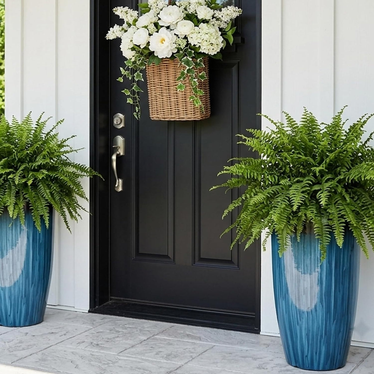 Pair of tall blue planters with lush ferns flanking a black front door and white siding.
