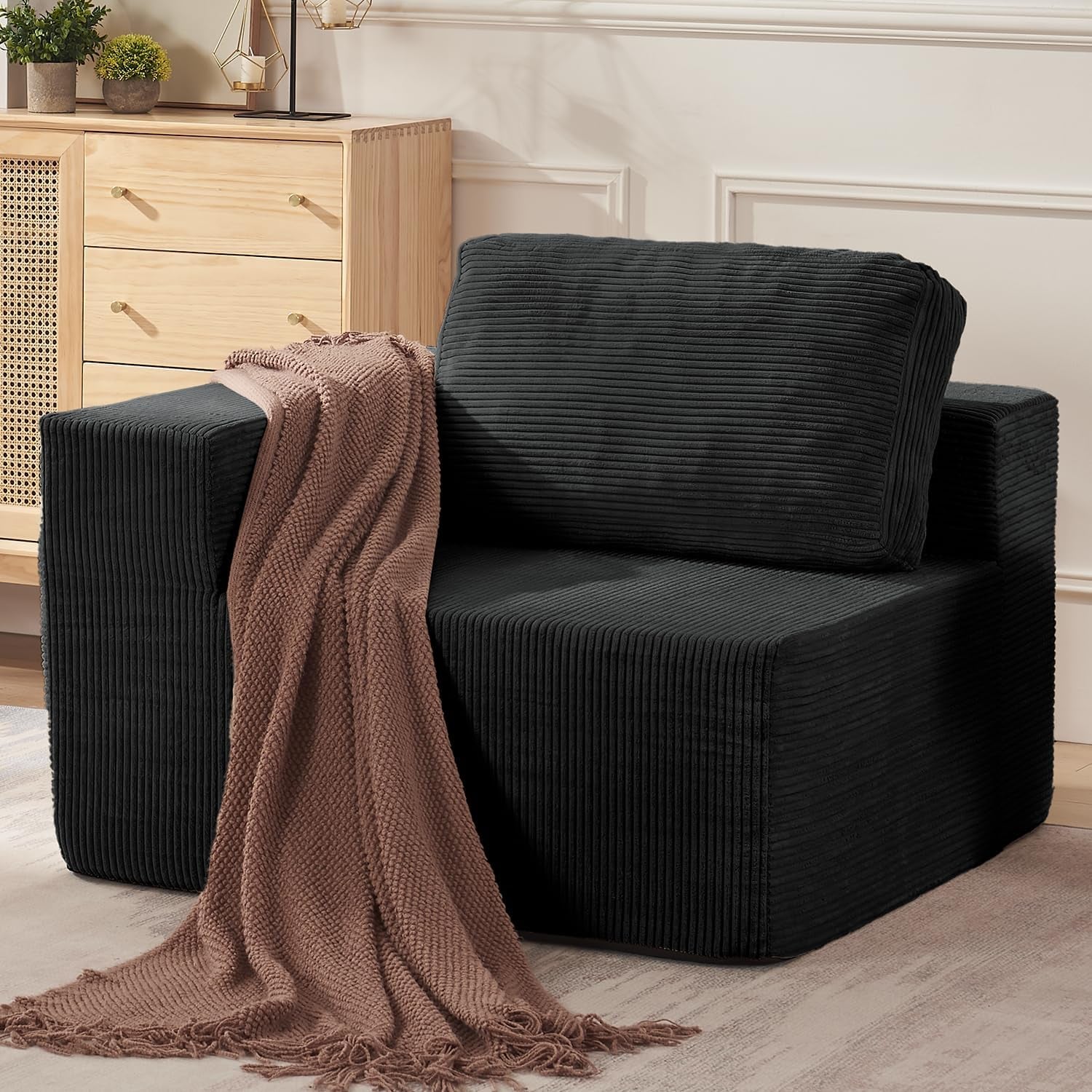 Close side view of a single black corduroy modular seat with a mauve knit throw draped over the arm.