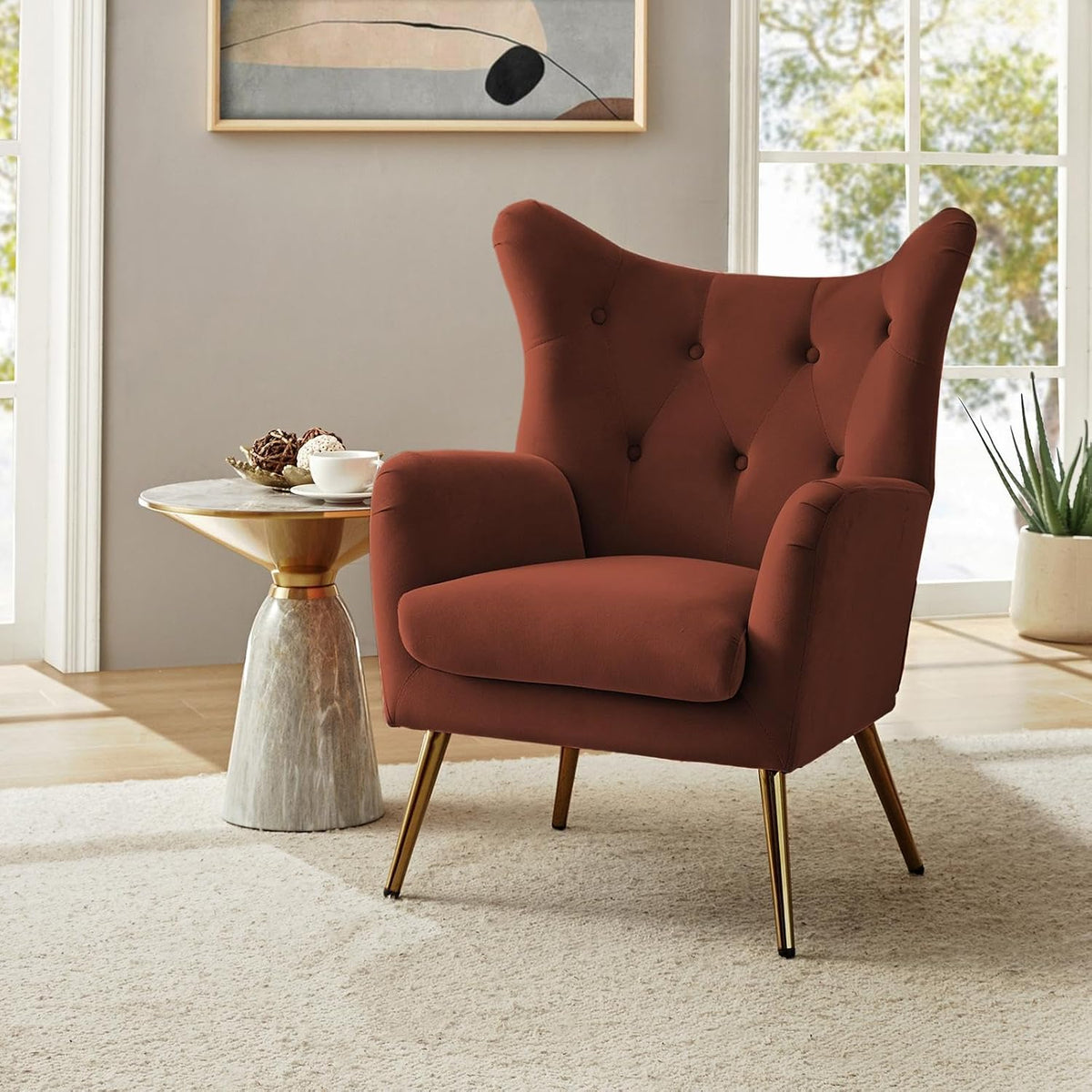 Rust-colored velvet wingback chair angled right beside a small round side table and window.