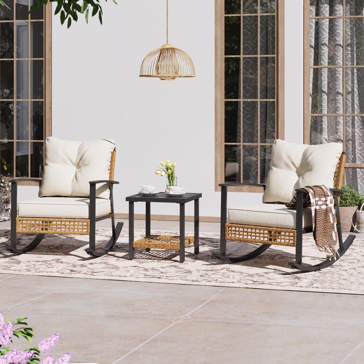Two cushioned rocking chairs flanking a small square coffee table on a patterned rug outside a home.