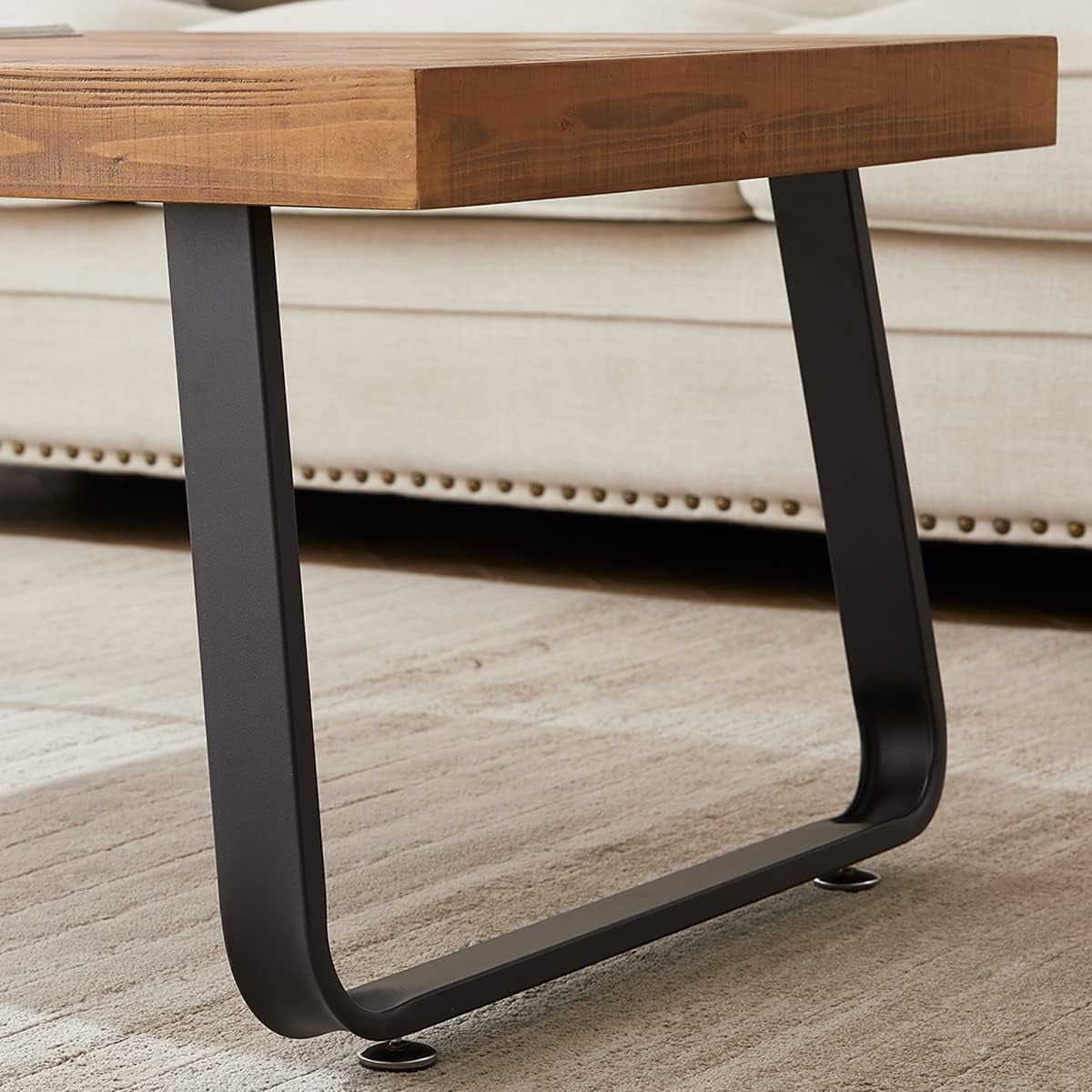 Close-up of the slanted U-shaped black metal leg and underside of the rustic fir tabletop beside a sofa