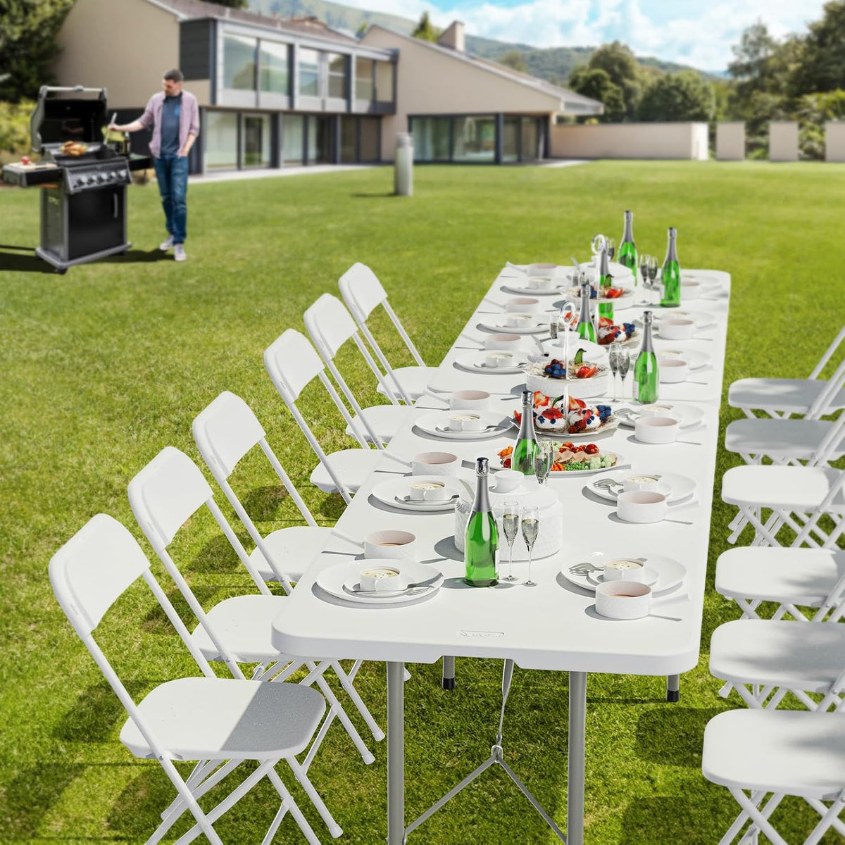 Long white folding table and matching chairs arranged on a lawn, set with plates and bottles for an outdoor meal.
