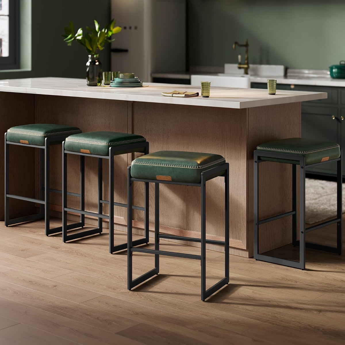 Four deep-green cushioned stools with visible contrast stitching placed along a light-wood island.