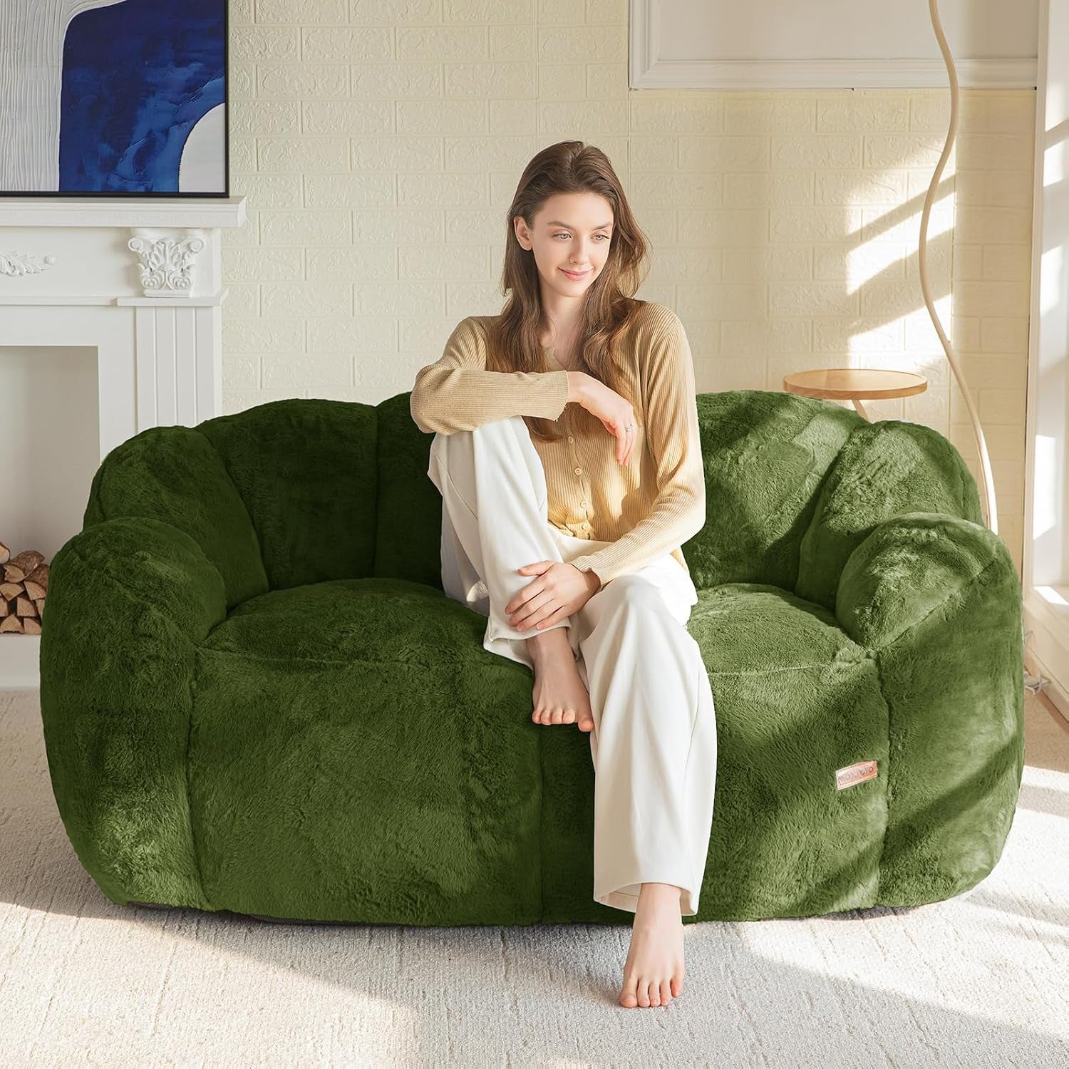 Woman sitting cross-legged on a large plush green floral-shaped bean bag sofa in a sunlit living room.