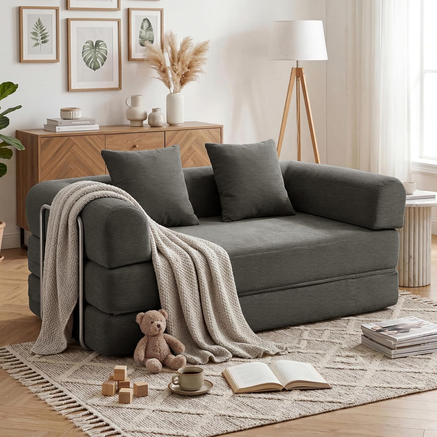 Charcoal gray corduroy sofa bed arranged as a loveseat with throw blanket and pillows in a styled living room