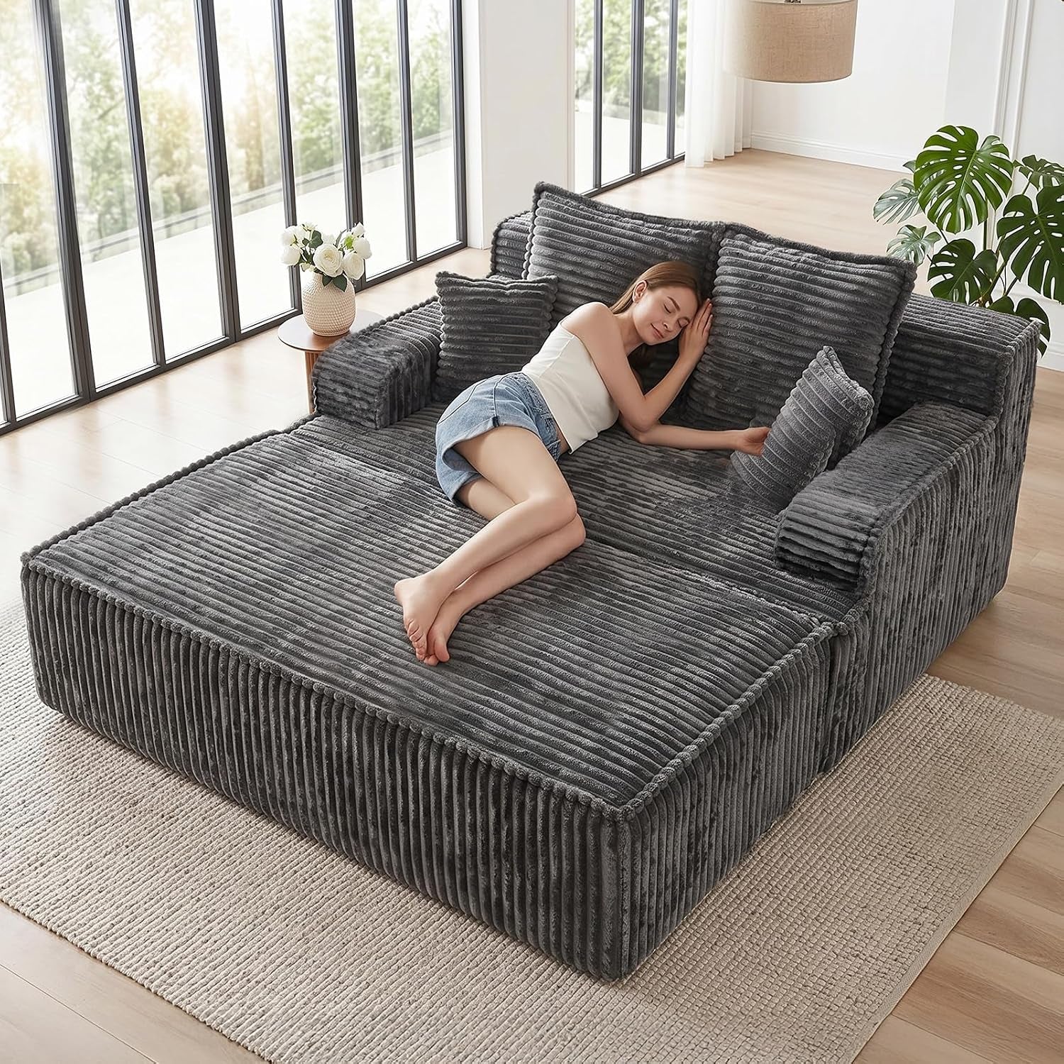 Angled view of a dark gray corduroy convertible chaise with armrests and a woman reclining