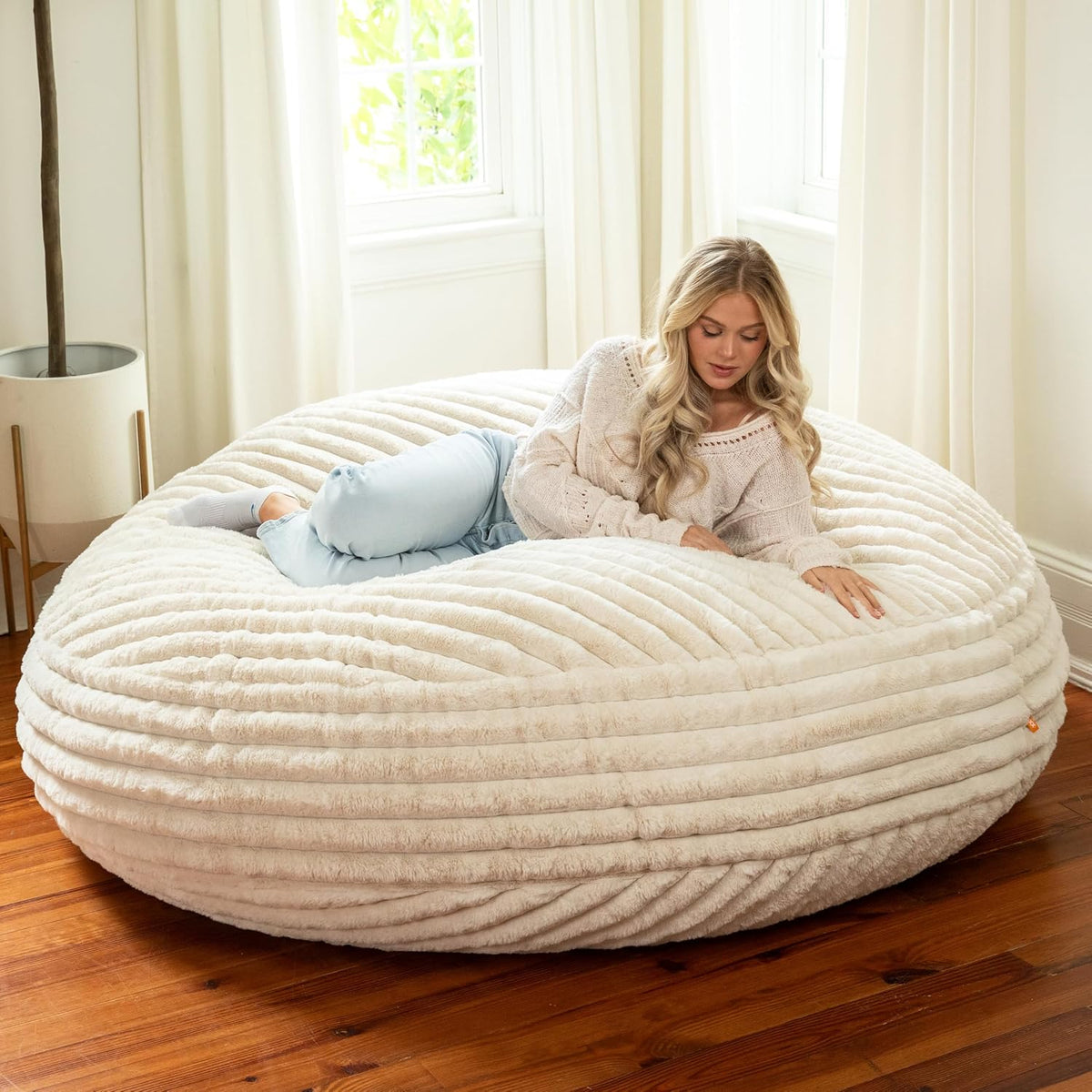 Cream ribbed round bean bag in a bright room with a woman reclining on it
