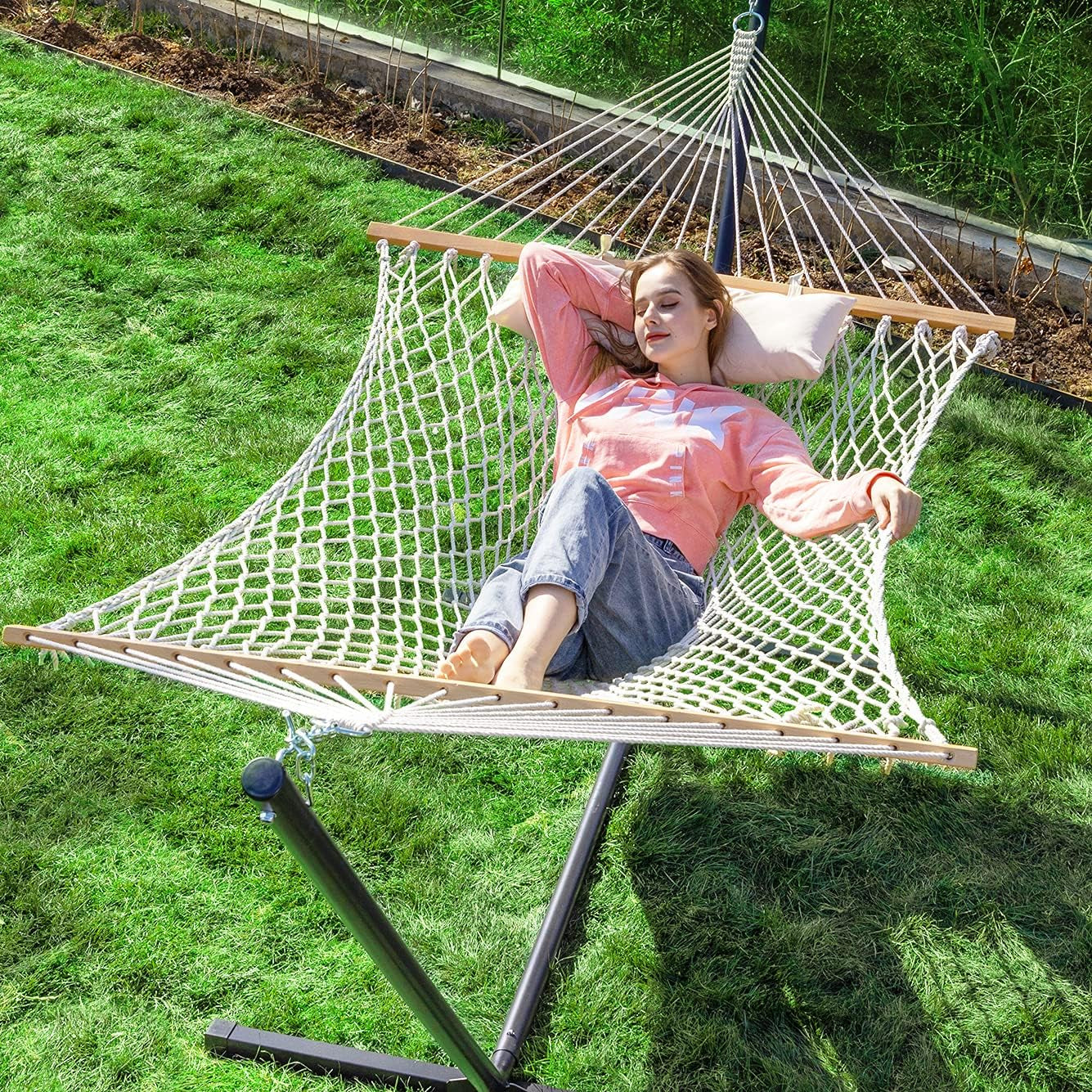Natural cotton-blend rope double hammock on black steel stand with pillow, angled top view in a grassy backyard