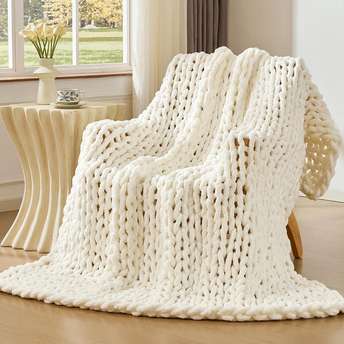 Creamy off-white chunky knit throw cascading over a lounge chair beside a sculpted side table