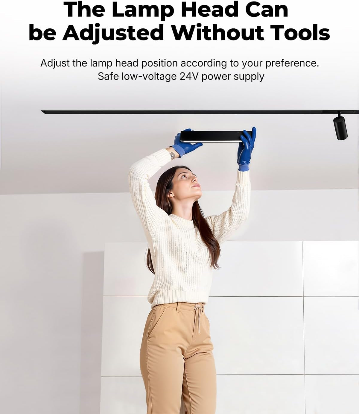 Woman standing on the floor reaching up to adjust a black magnetic track light head installed in a ceiling track.
