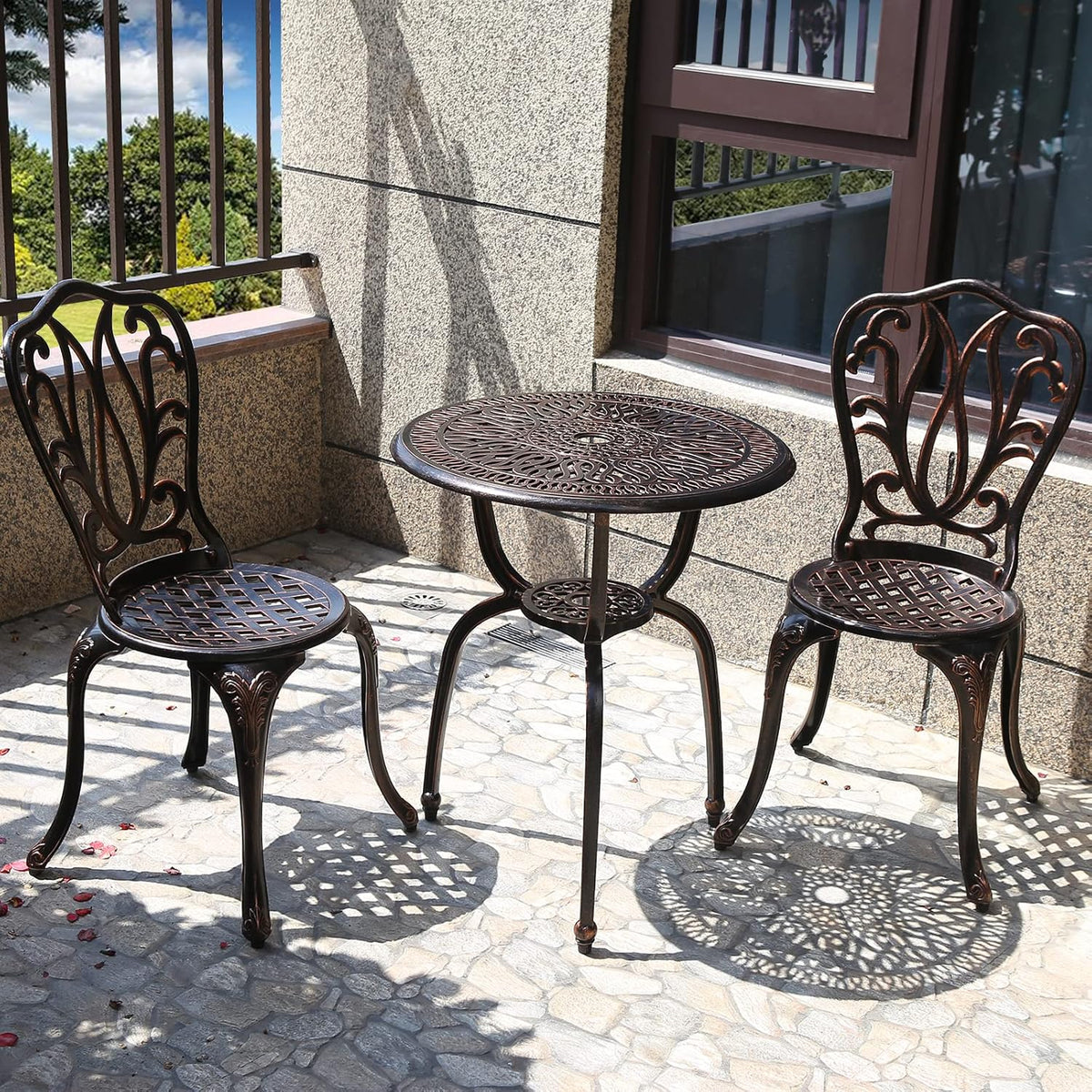 Close view of bronze bistro table and two chairs showing ornate tabletop pattern and shadows.