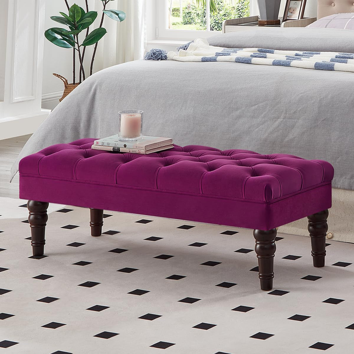 Front view of a deep magenta tufted bench with turned dark wood legs on a black-diamond patterned rug, candle and books on