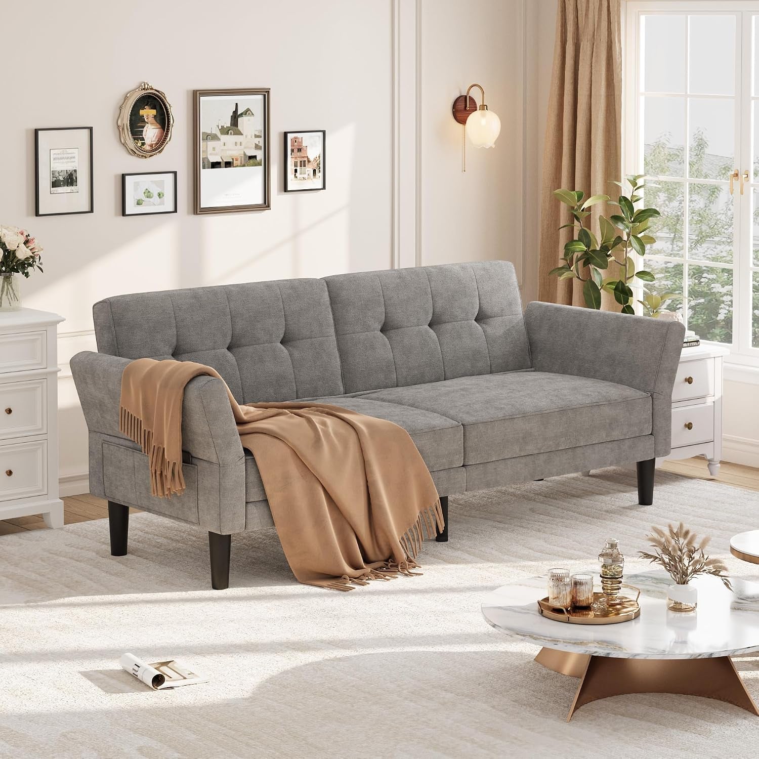 Three-seat gray chenille futon sofa with tufted back and beige throw in a sunlit living room.