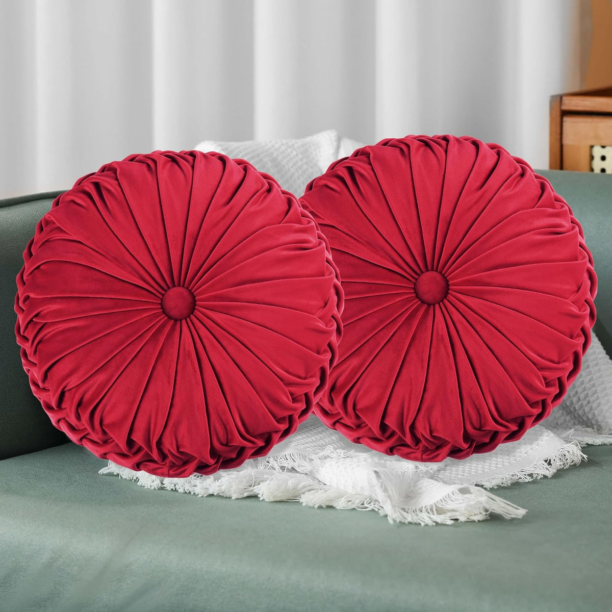 Pair of round ruched throw pillows in bright red arranged on a green upholstered seat.