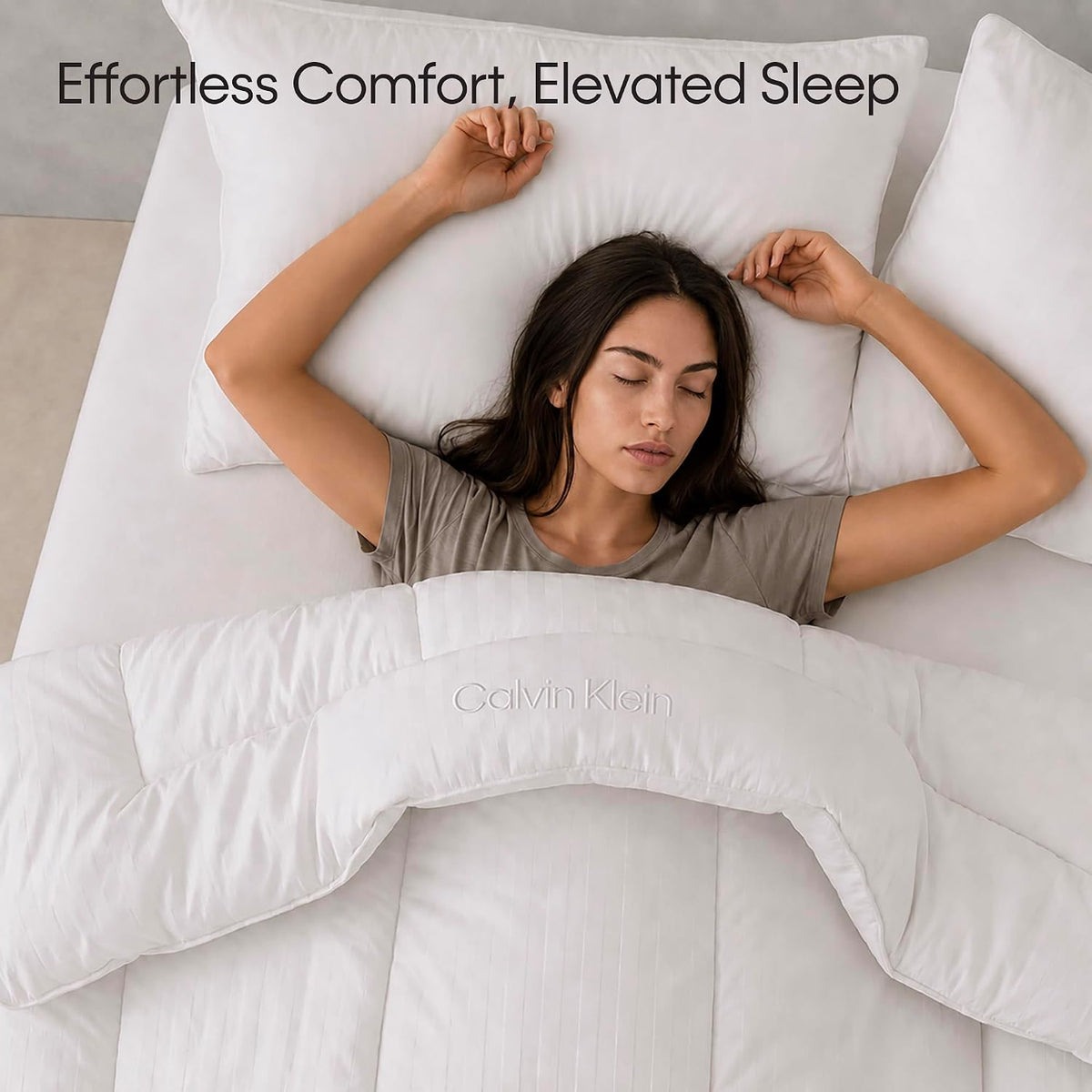 Woman sleeping on her back under a white comforter with matching pillows, overhead angled view