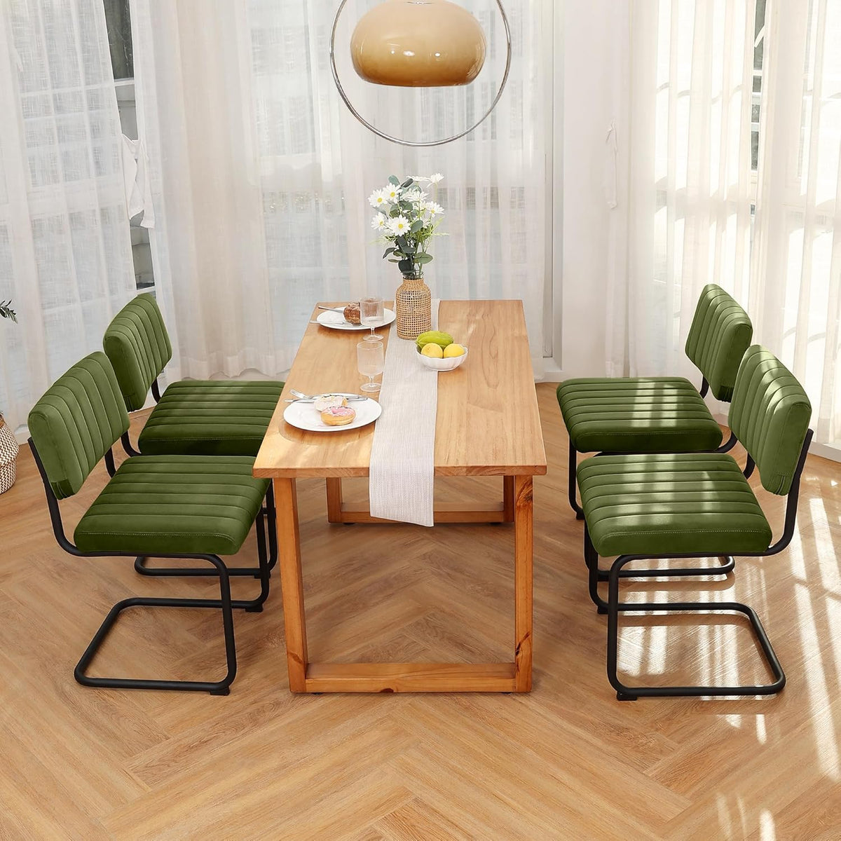 Dining table seen from above with four green velvet cantilever chairs, place settings and pendant light