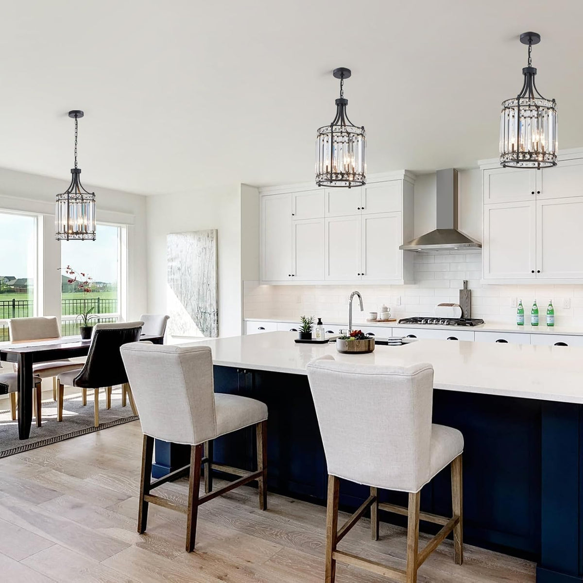 Three black crystal pendant chandeliers hung above a large white kitchen island with navy base and beige barstools.