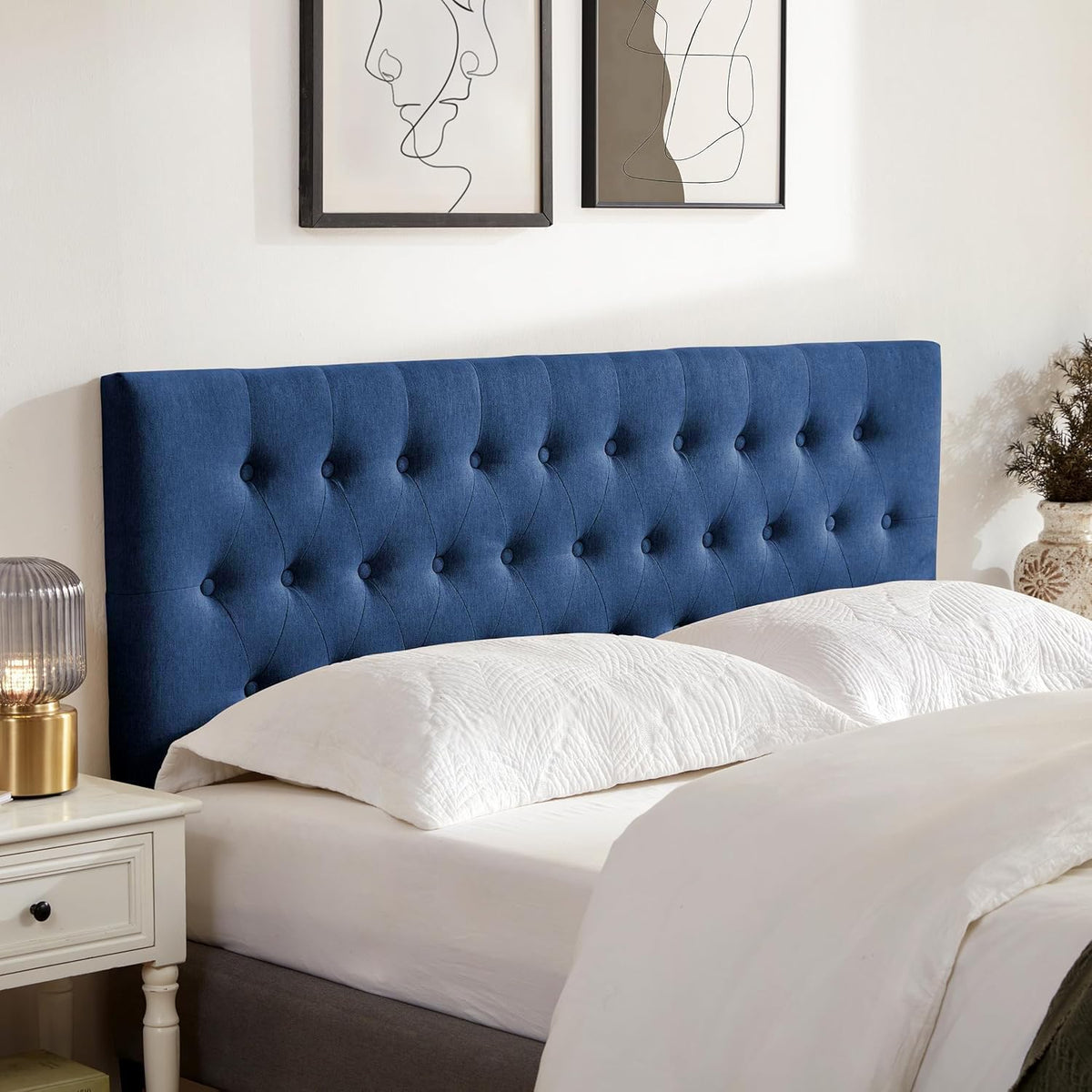 Deep navy blue tufted headboard shown at an angle with white pillows and nightstand lamp.